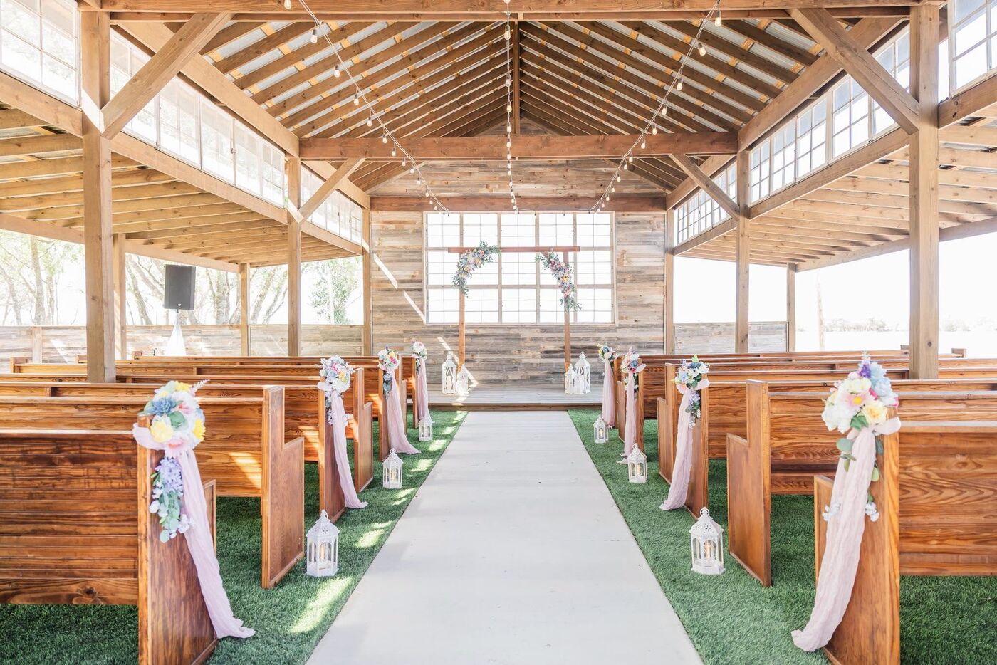 Aisle of the open-air chapel lined with wooden pews and soft florals