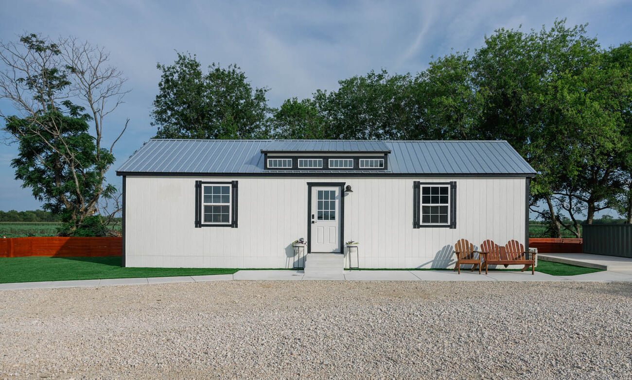 White cabin with a metal roof and chairs out front